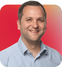Headshot of Oliver Sinclair, a smiling man wearing a light blue shirt, set against a red and gradient background.