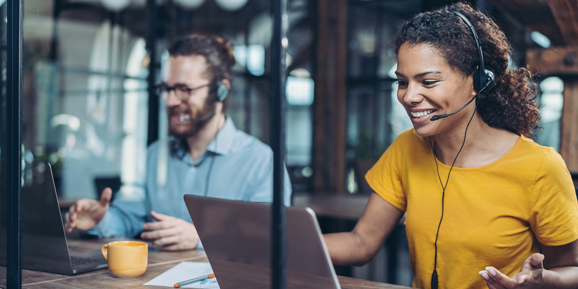woman and man working on laptop with headsets on 